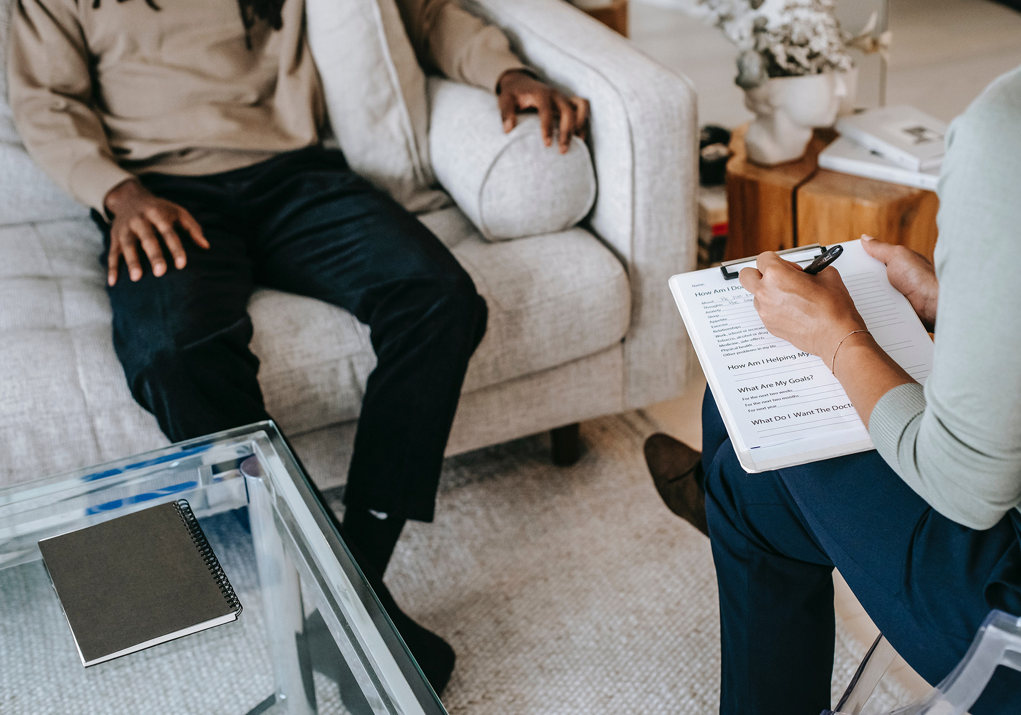 female with clipboard talking to male seated on couch